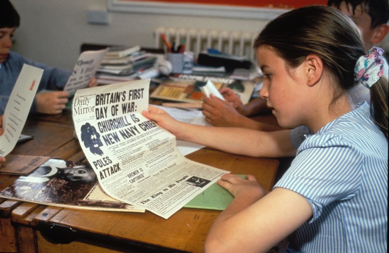 History studies at primary school Pupils studying Second World War by reading old newspaper UK